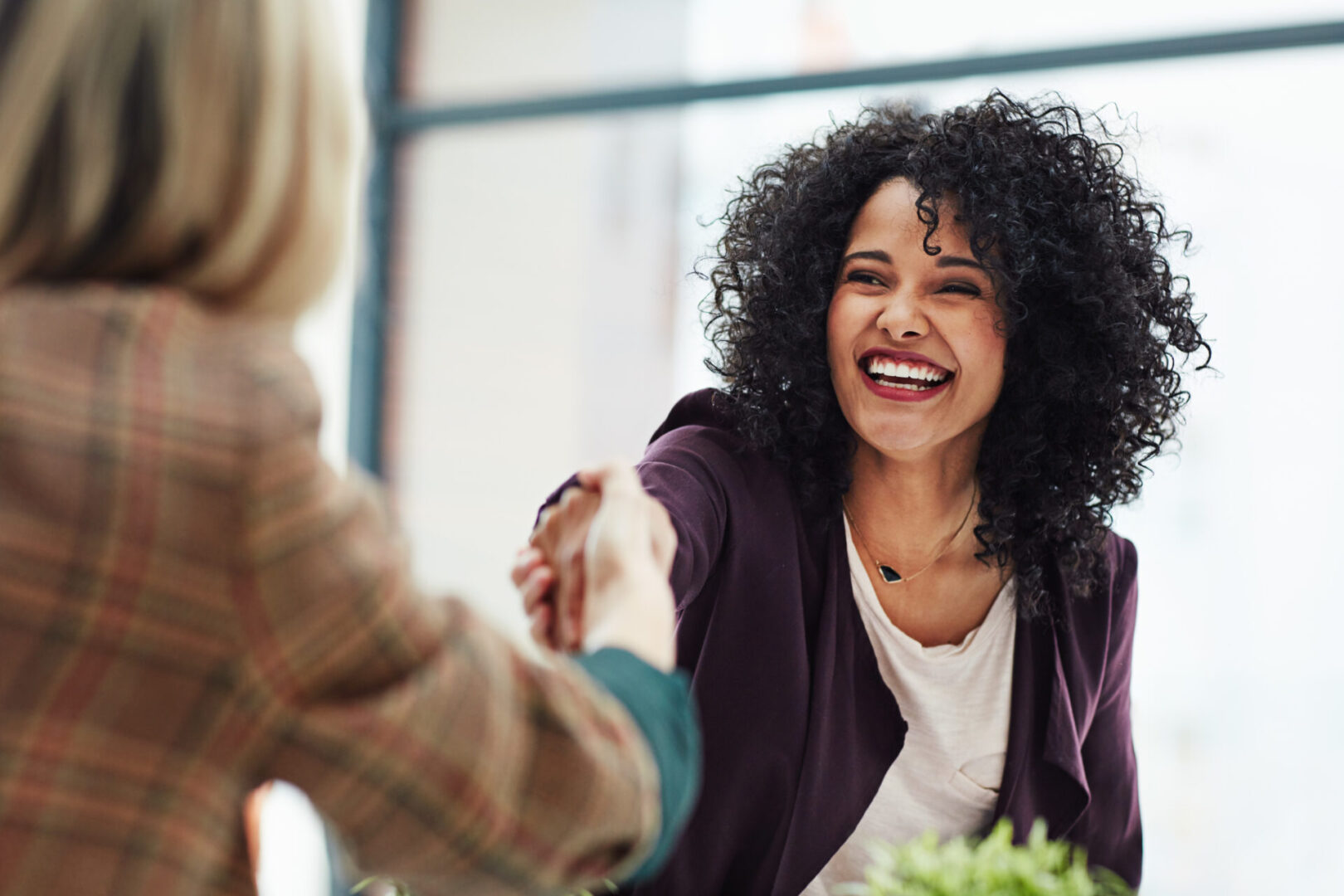 Woman smiling while shaking hands in office.